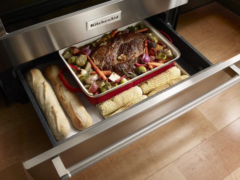 Open warming drawer with bread, a roast and vegetables inside Open warming drawer with bread, a roast and vegetables inside