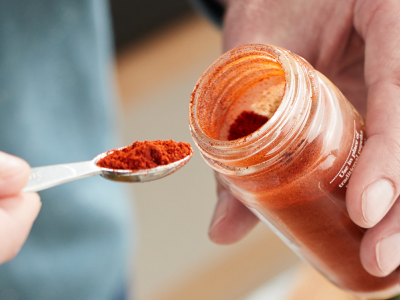 A closeup of hands holding a spoonful of red seasoning and the container.