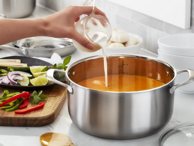 A closeup of a hand pouring milk into a pot of soup.