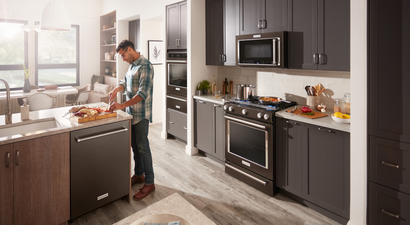 A man chopping ingredients in front of a KitchenAid® slide-in range and microwave A man chopping ingredients in front of a KitchenAid® slide-in range and microwave