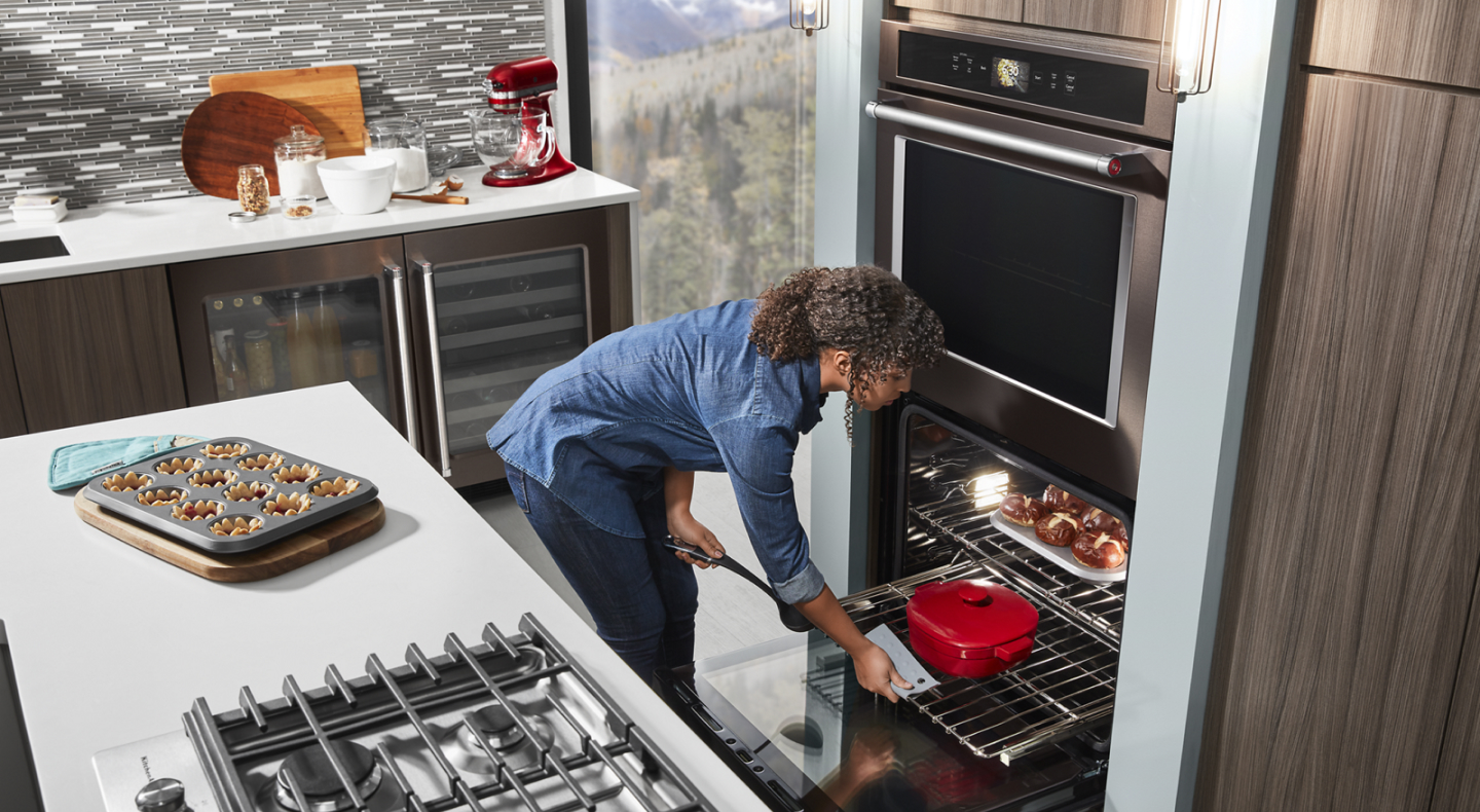 Person sliding a casserole dish out from the bottom rack of a KitchenAid® double wall oven