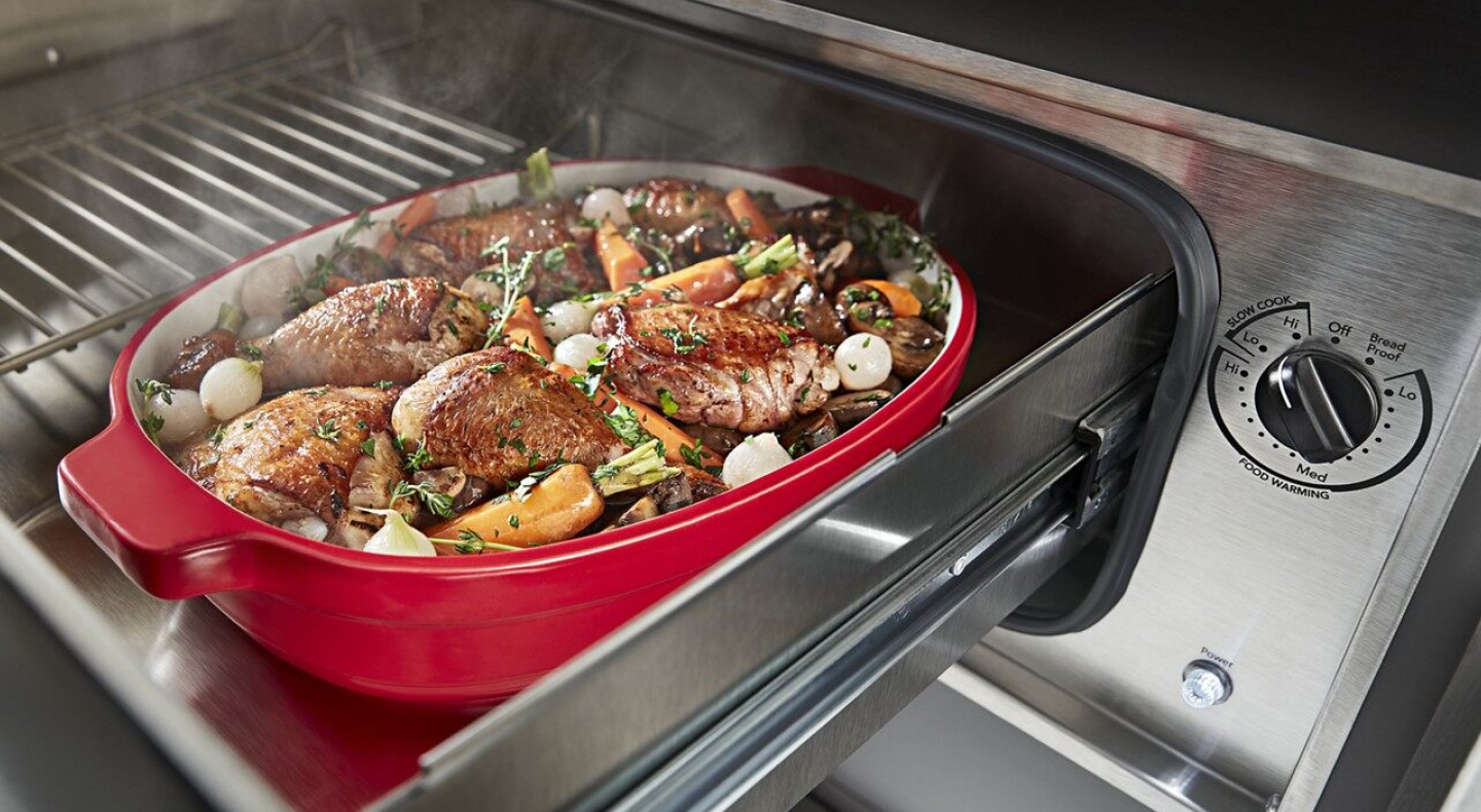 Roasted chicken thighs and vegetables in a casserole dish inside of a warming drawer  Roasted chicken thighs and vegetables in a casserole dish inside of a warming drawer