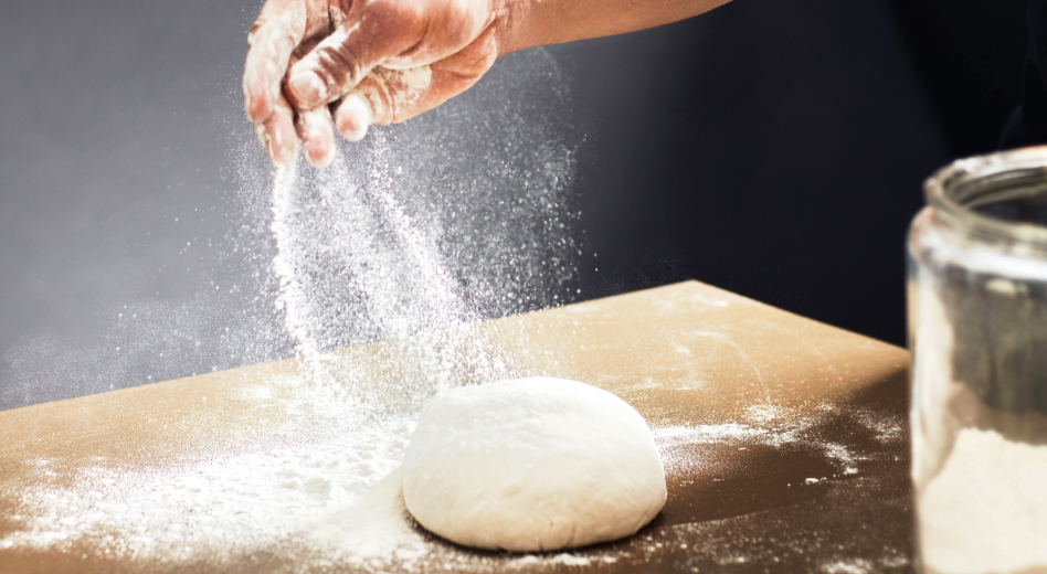 Hand sprinkling flour on ball of dough Hand sprinkling flour on ball of dough