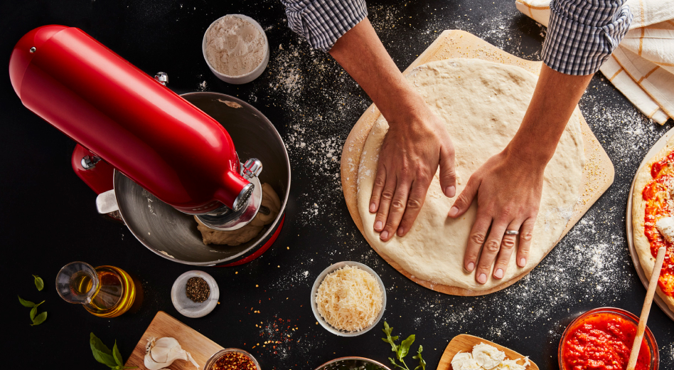 Two hands pushing down circle of dough on pizza peel next to red KitchenAid® Stand Mixer  Two hands pushing down circle of dough on pizza peel next to red KitchenAid® Stand Mixer
