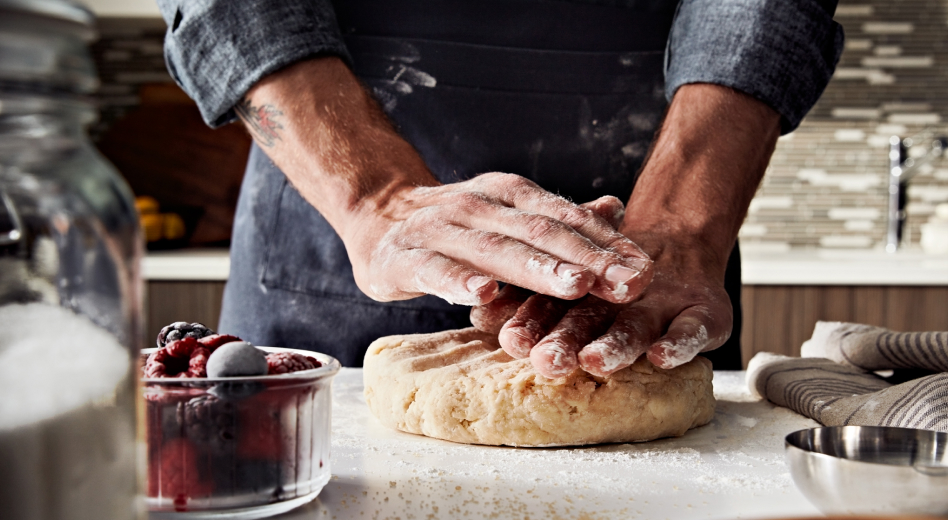 Two hands covered in flour pressing down on a circle of dough on top of a counter