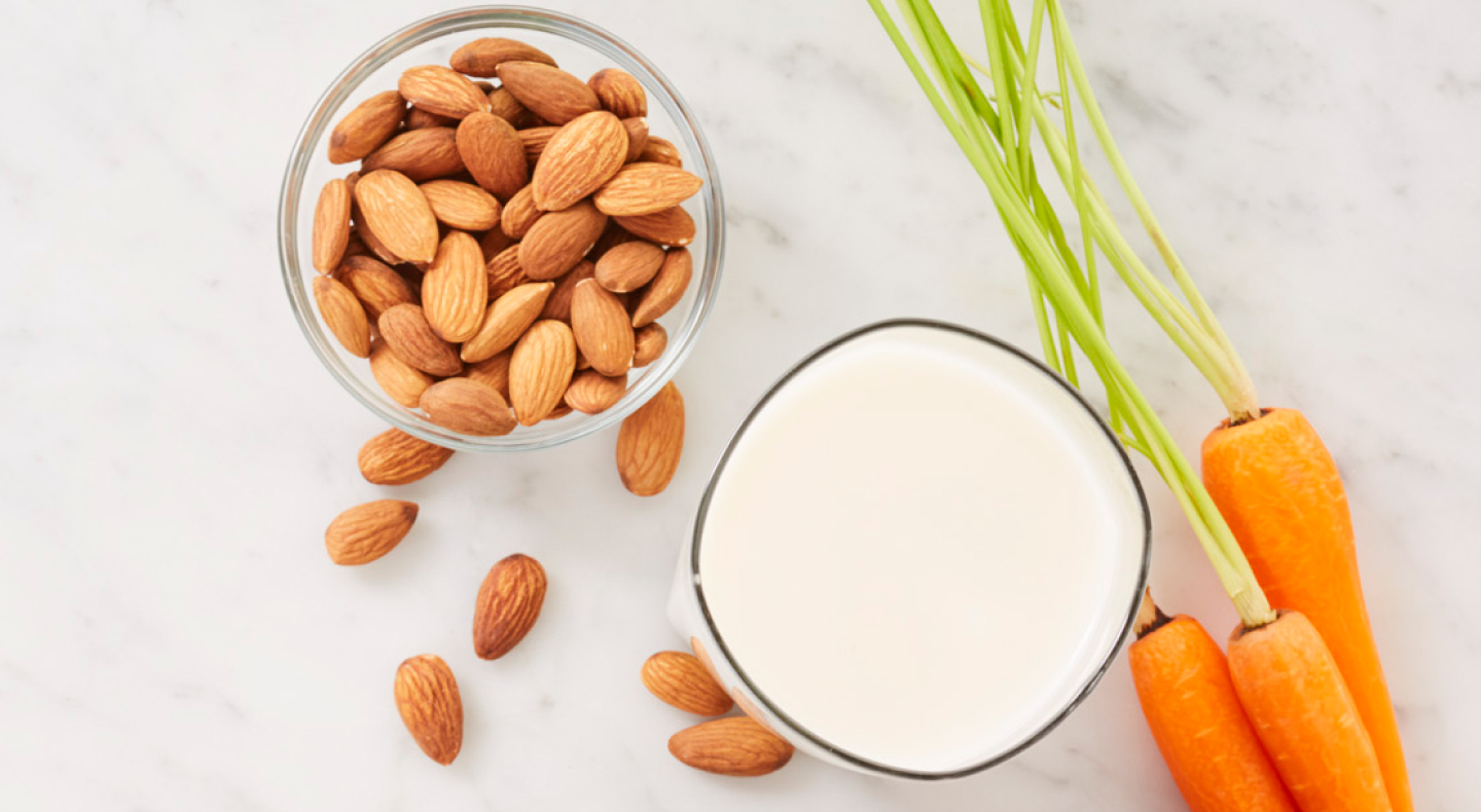 Carrots next to a bowl of almonds and glass of milk