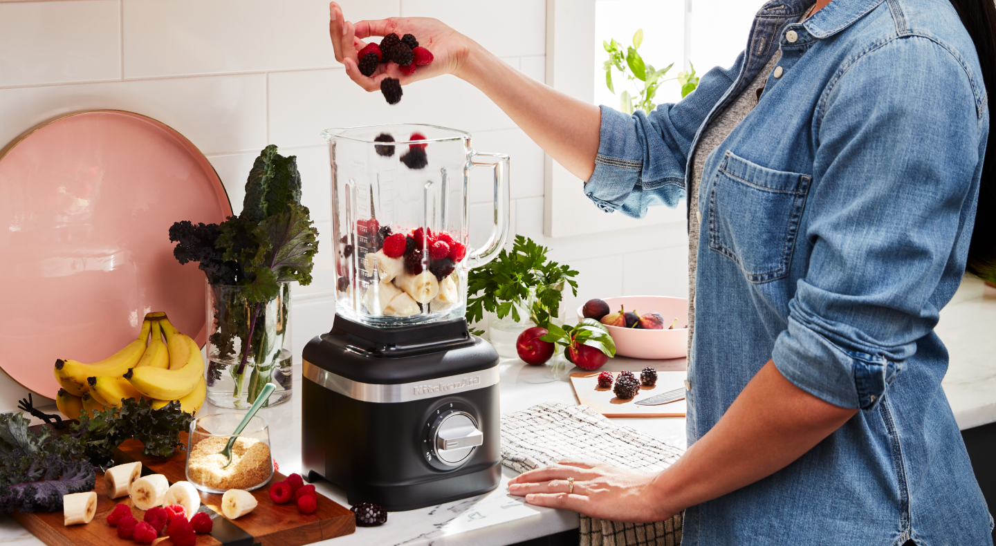 Person adding fruit to a blender Person adding fruit to a blender