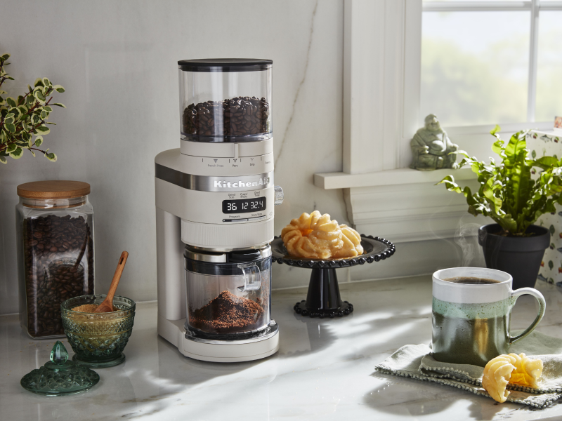 White KitchenAid® burr grinder next to a cup of coffee and pastries White KitchenAid® burr grinder next to a cup of coffee and pastries