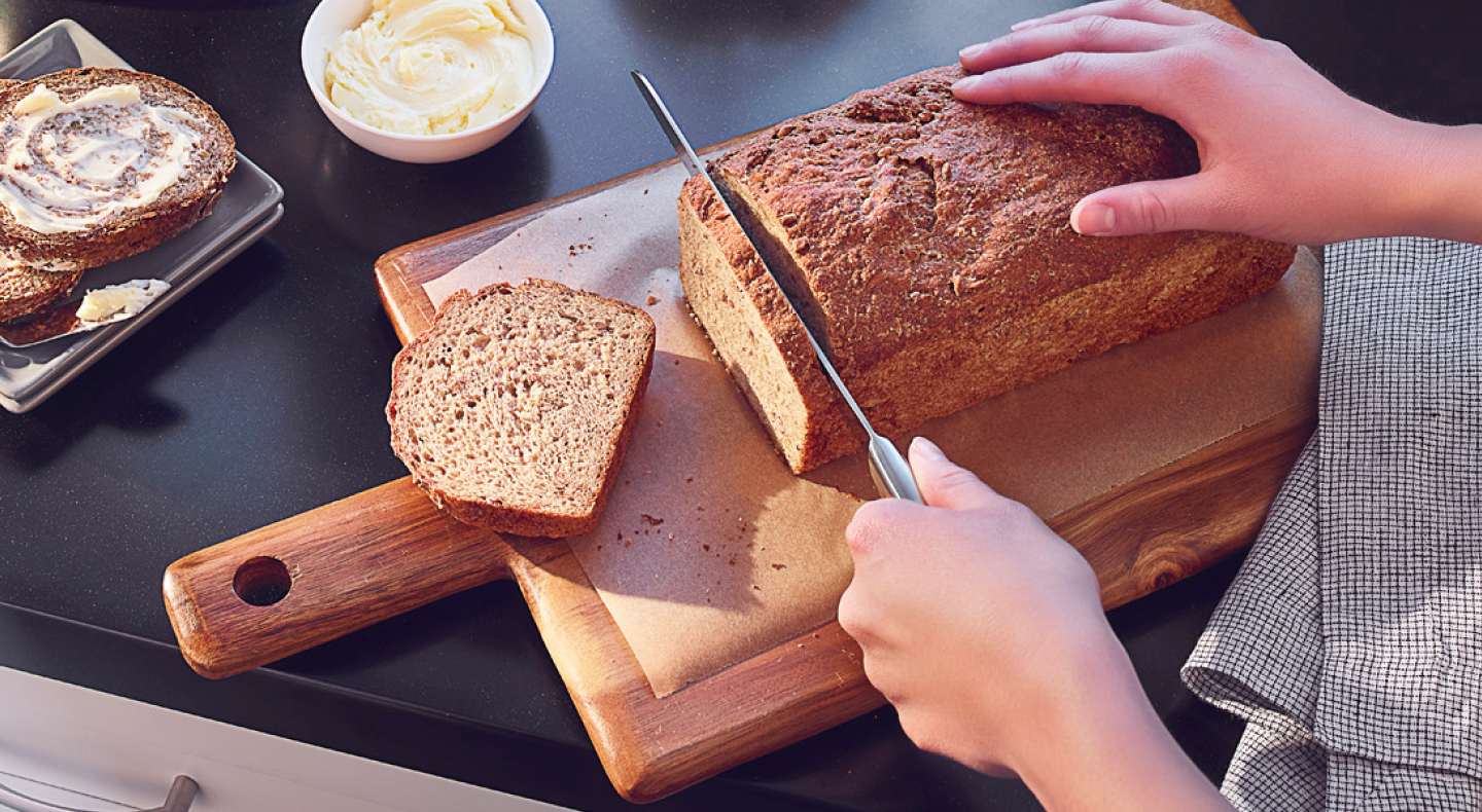 Person slicing banana bread on wooden cutting board Person slicing banana bread on wooden cutting board