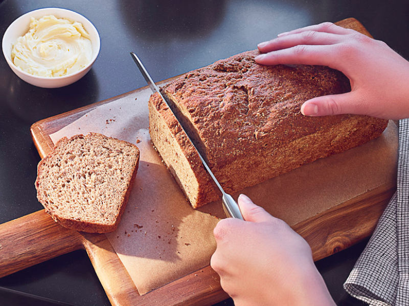 Person slicing banana bread on wooden cutting board