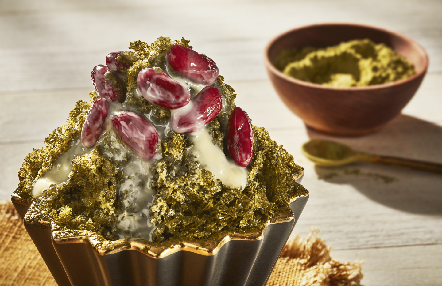 Shaved ice dessert with red beans and matcha powder beside bowl of match powder Shaved ice dessert with red beans and matcha powder beside bowl of match powder
