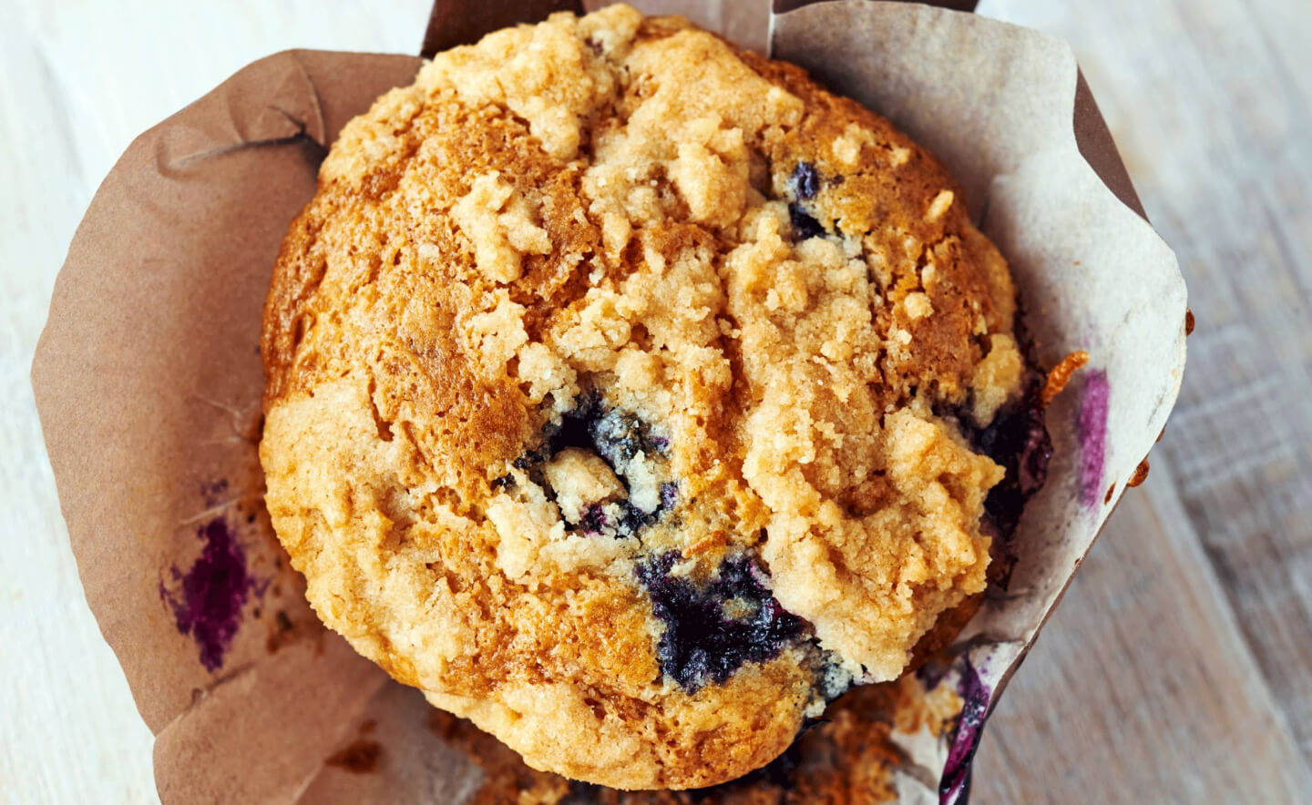 Birds-eye view of a streusel-topped blueberry muffin inside of a decorative liner Birds-eye view of a streusel-topped blueberry muffin inside of a decorative liner