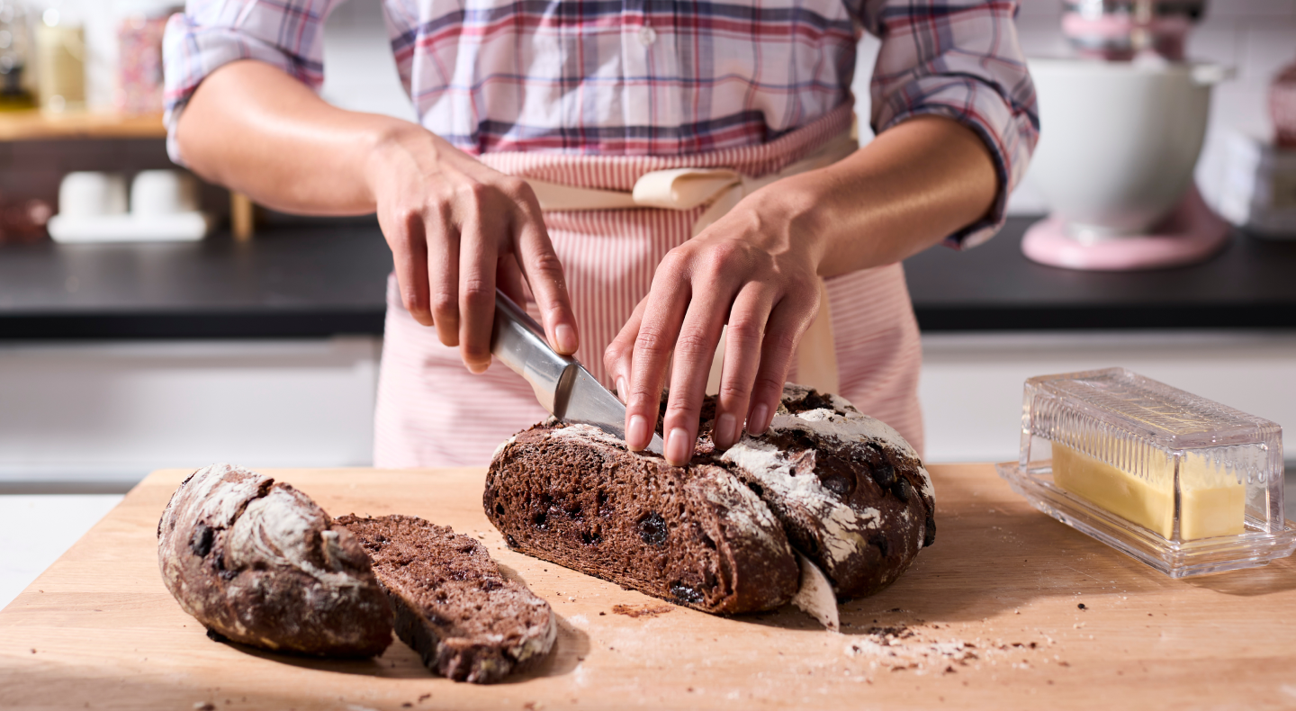 Person slicing a loaf of bread on a wooden cutting board Person slicing a loaf of bread on a wooden cutting board