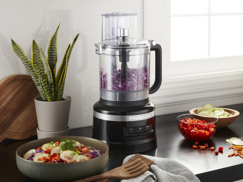 KitchenAid® food processor with purple cabbage next to a chopped salad and the ingredients in a modern kitchen. KitchenAid® food processor with purple cabbage next to a chopped salad and the ingredients in a modern kitchen.