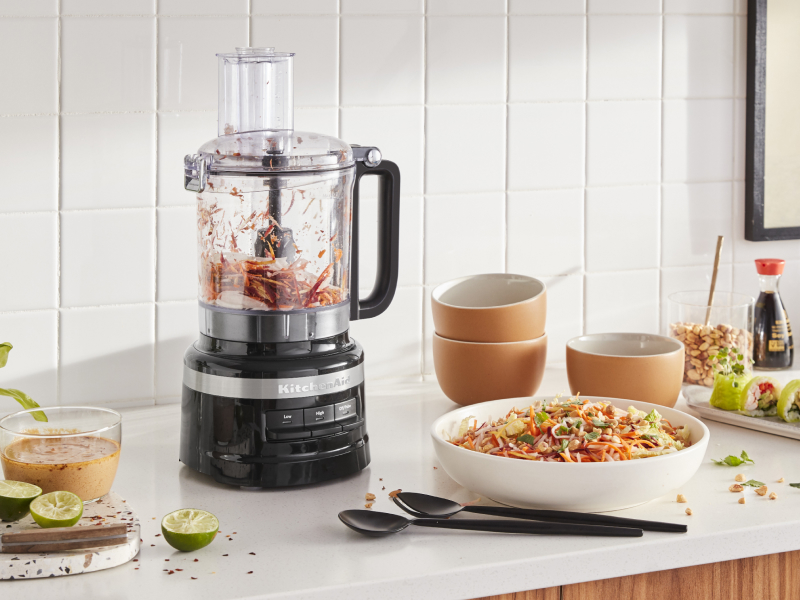 KitchenAid® food processor with chopped vegetables next to a chopped salad and freshly made salad dressing in a modern kitchen. KitchenAid® food processor with chopped vegetables next to a chopped salad and freshly made salad dressing in a modern kitchen.