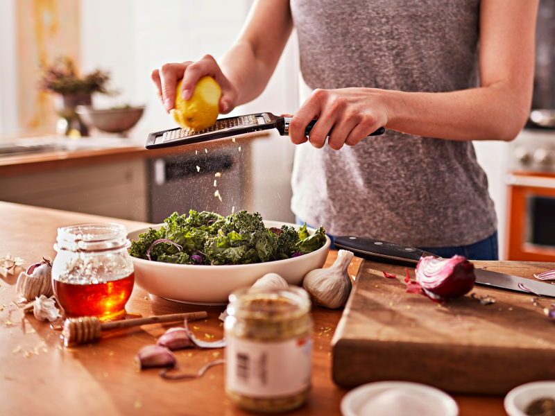 A woman shredding lemon peel onto a chopped salad in a modern kitchen. A woman shredding lemon peel onto a chopped salad in a modern kitchen.