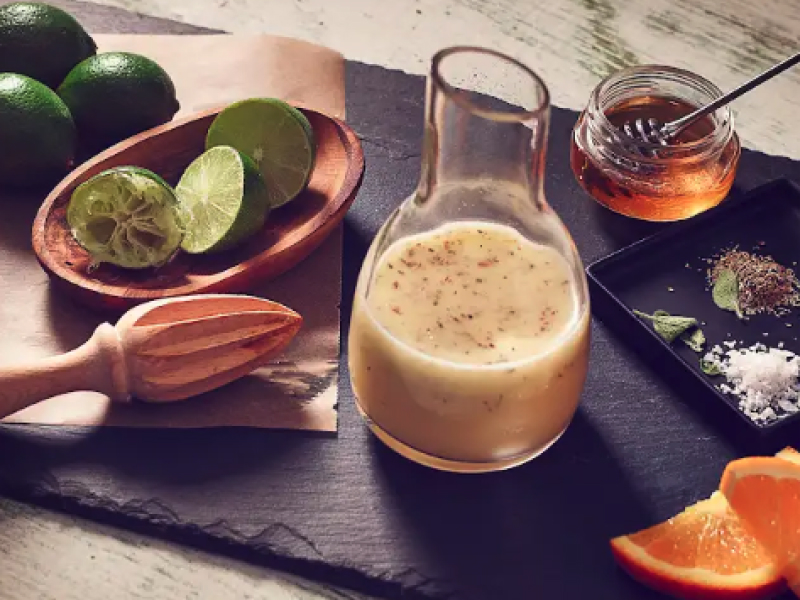 Homemade salad dressing in a glass serving jar next to limes and other ingredients.