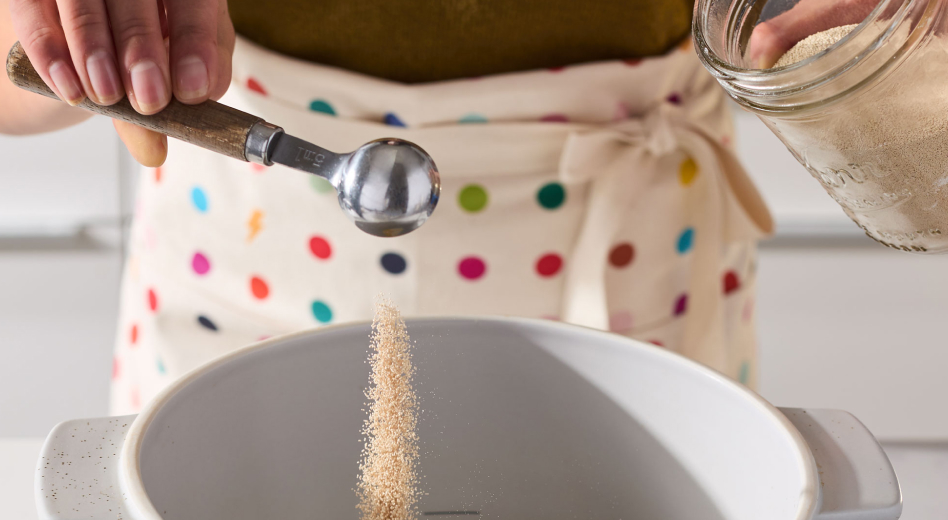 Person adding cinnamon roll bread ingredients into a bowl Person adding cinnamon roll bread ingredients into a bowl