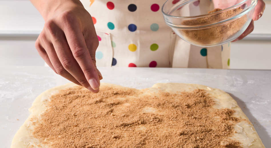 Person sprinkling filling onto cinnamon roll bread dough Person sprinkling filling onto cinnamon roll bread dough