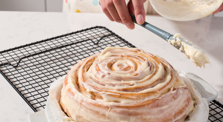 Person icing cinnamon roll bread on cooling rack Person icing cinnamon roll bread on cooling rack