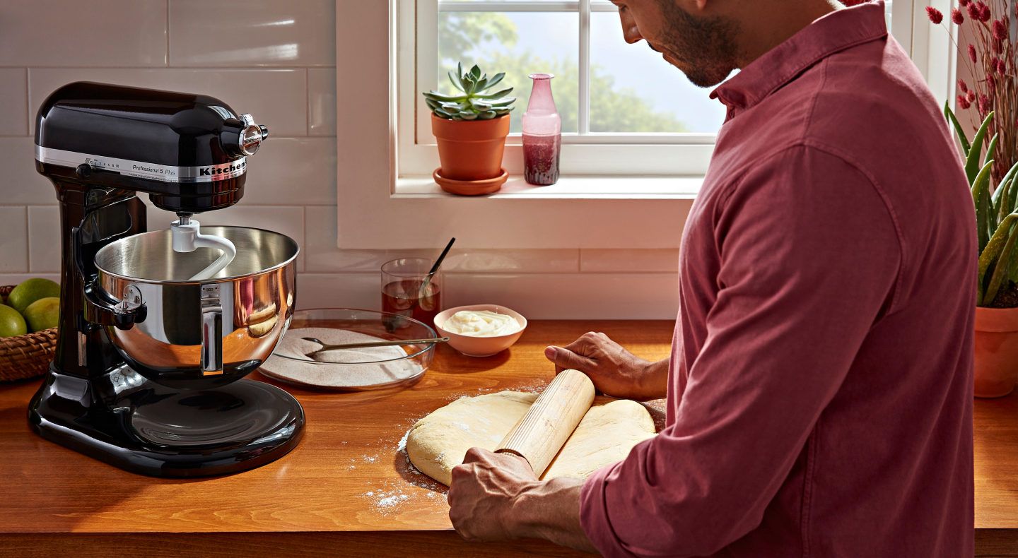 Person rolling out dough next to a black KitchenAid® stand mixer Person rolling out dough next to a black KitchenAid® stand mixer