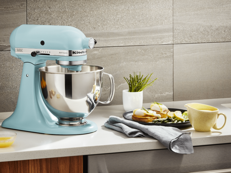 A stand mixer sitting next to a plate of eggs benedict A stand mixer sitting next to a plate of eggs benedict