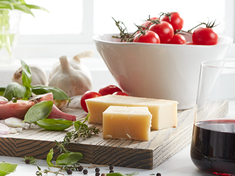 Wood block cutting board with cheese blocks and a bowl of vine tomatoes on top