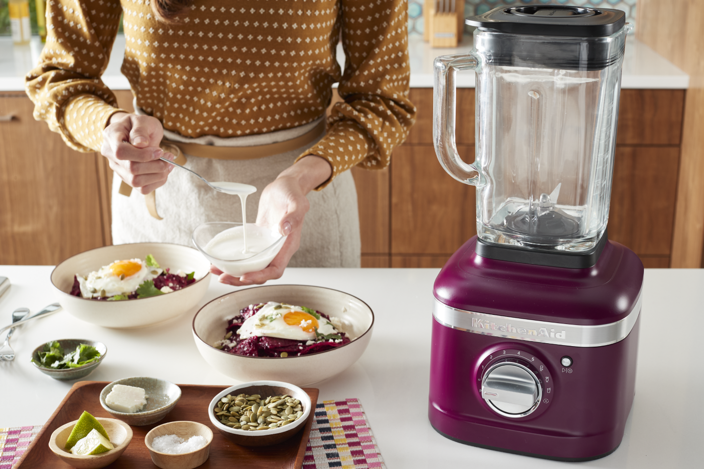 Person putting dressing on a meal next to KitchenAid® blender Person putting dressing on a meal next to KitchenAid® blender