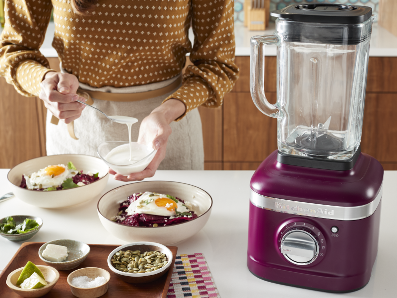 Person putting dressing on a meal next to KitchenAid® blender Person putting dressing on a meal next to KitchenAid® blender