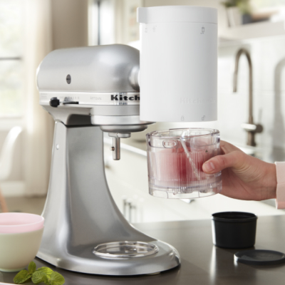 Hand holding a glass cup under a KitchenAid® Stand Mixer with Shave Ice Attachment
