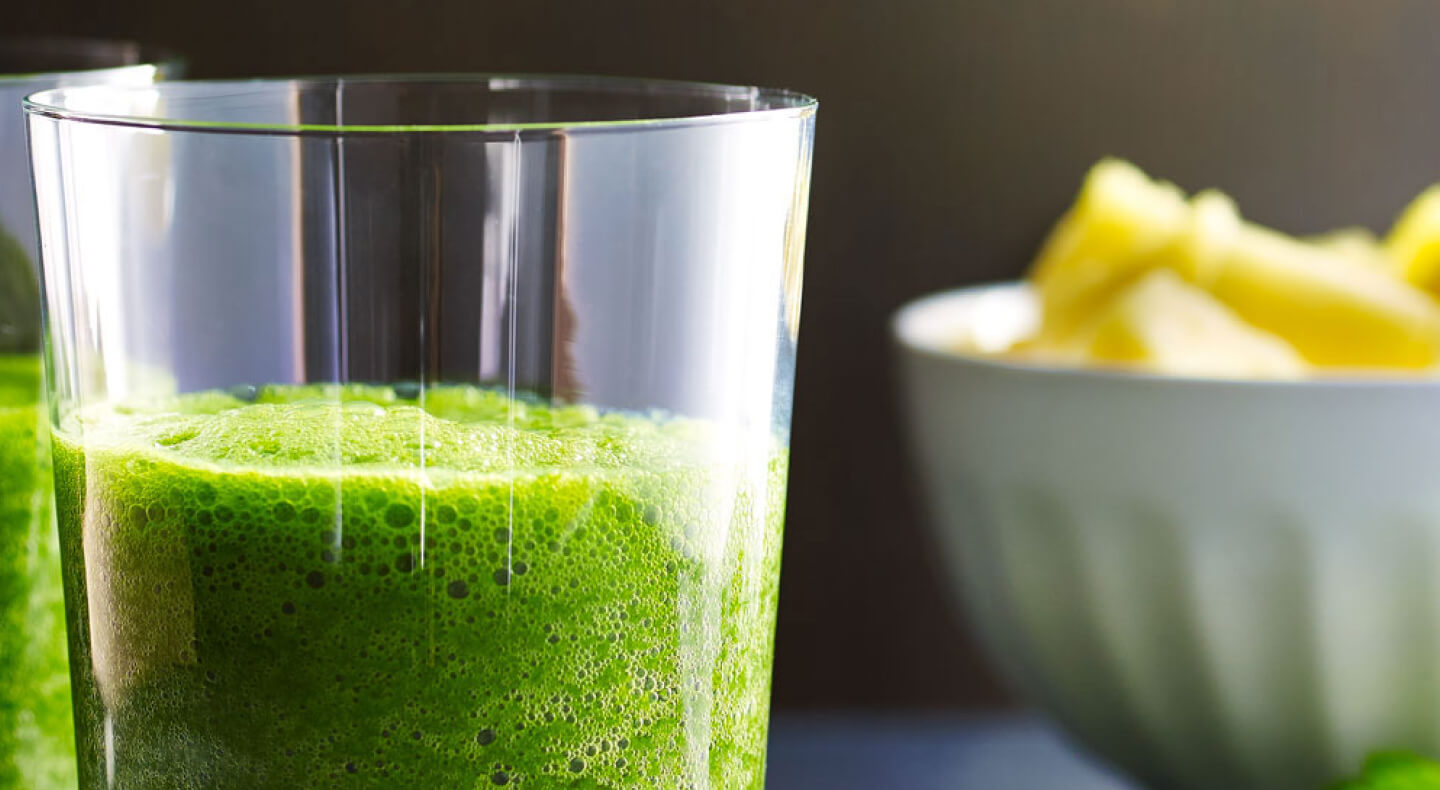 Green juice in a glass next to a bowl of sliced pineapples Green juice in a glass next to a bowl of sliced pineapples