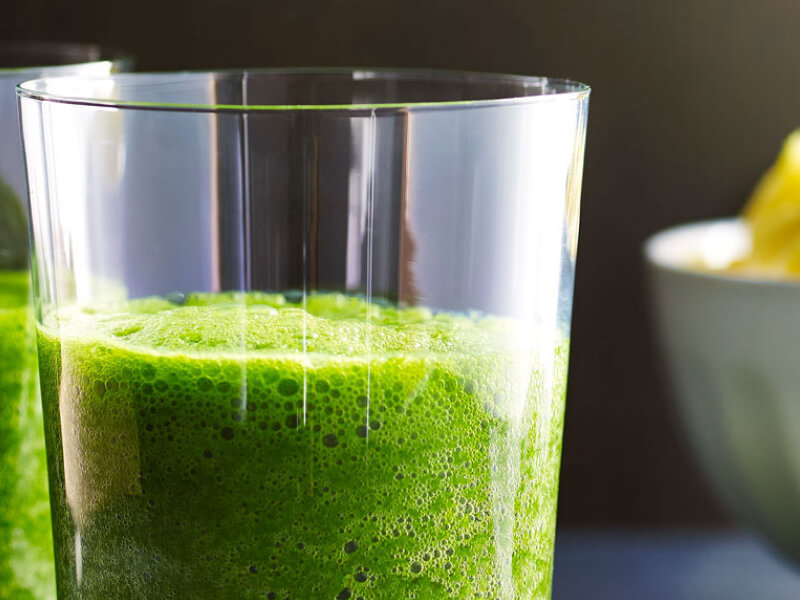 Green juice in a glass next to a bowl of sliced pineapples Green juice in a glass next to a bowl of sliced pineapples