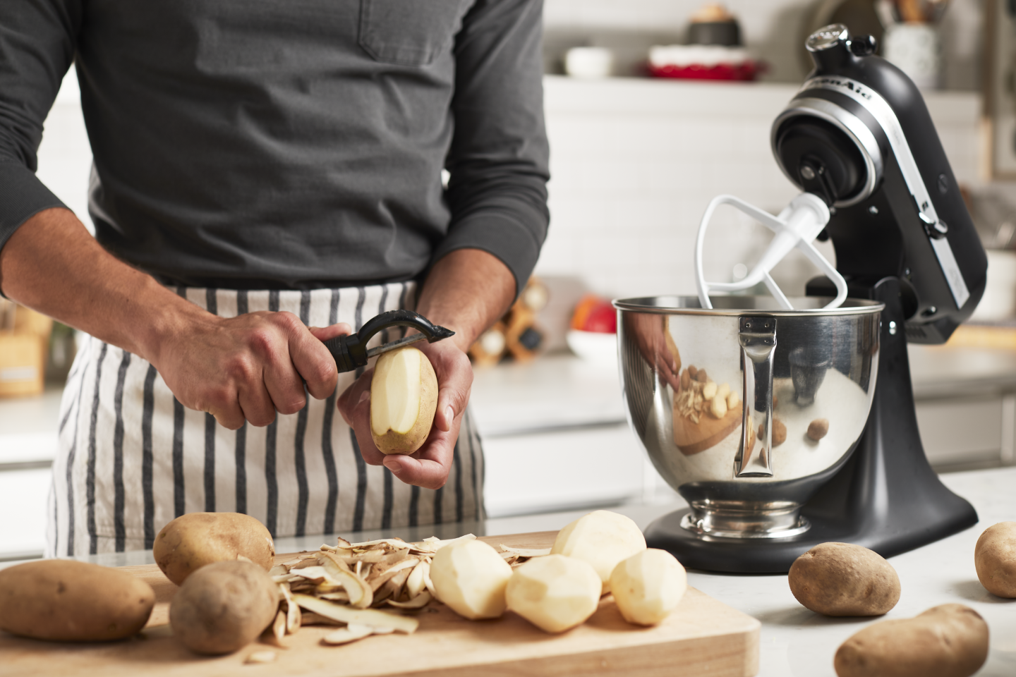 Person peeling potatoes next to a stand mixer Person peeling potatoes next to a stand mixer