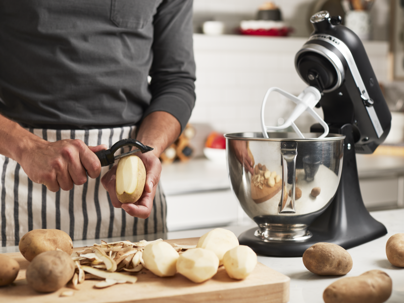 Person peeling potatoes next to a stand mixer Person peeling potatoes next to a stand mixer