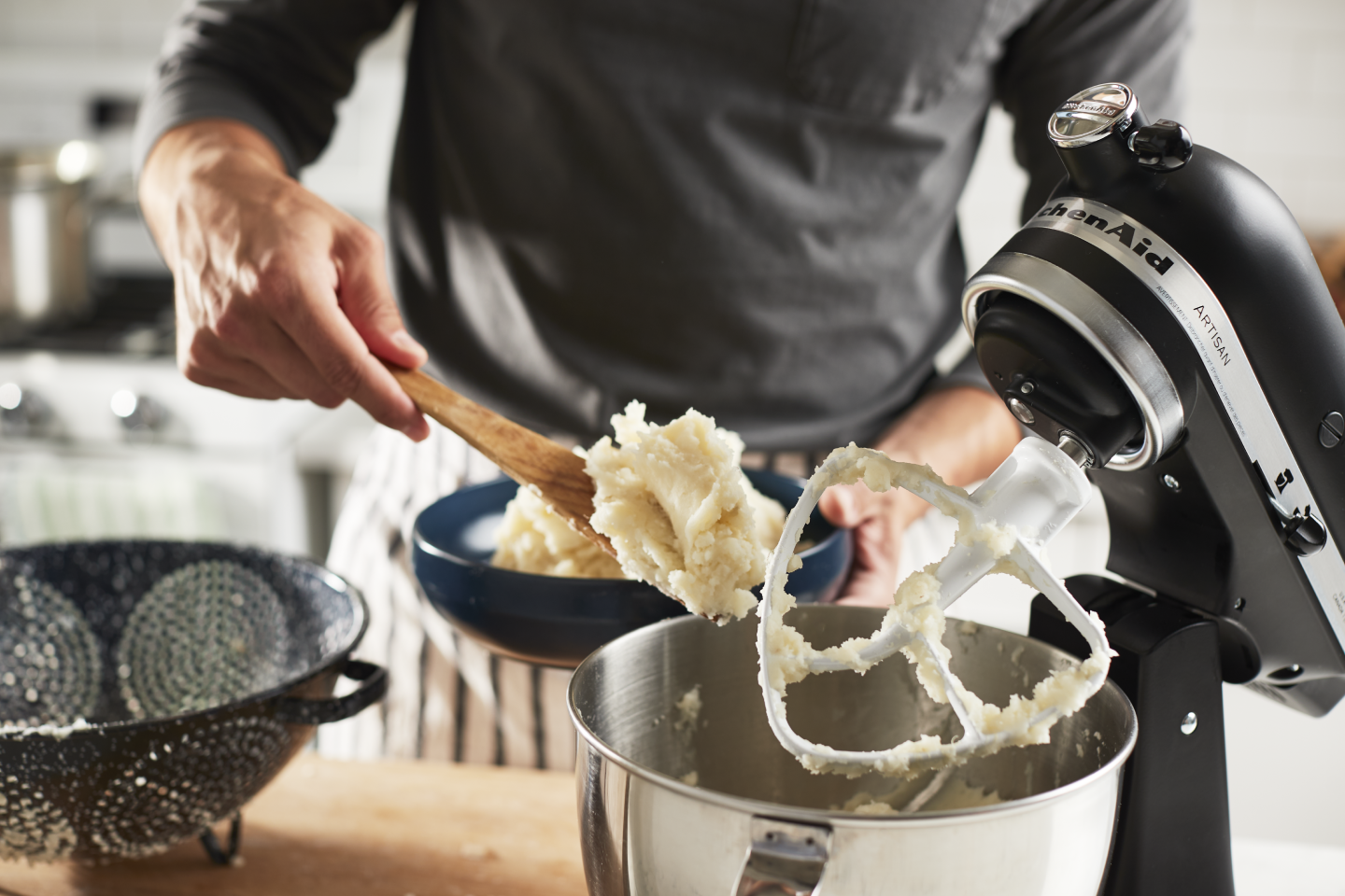Man scooping mashed potatoes out of a stand mixer into a serving bowl Man scooping mashed potatoes out of a stand mixer into a serving bowl