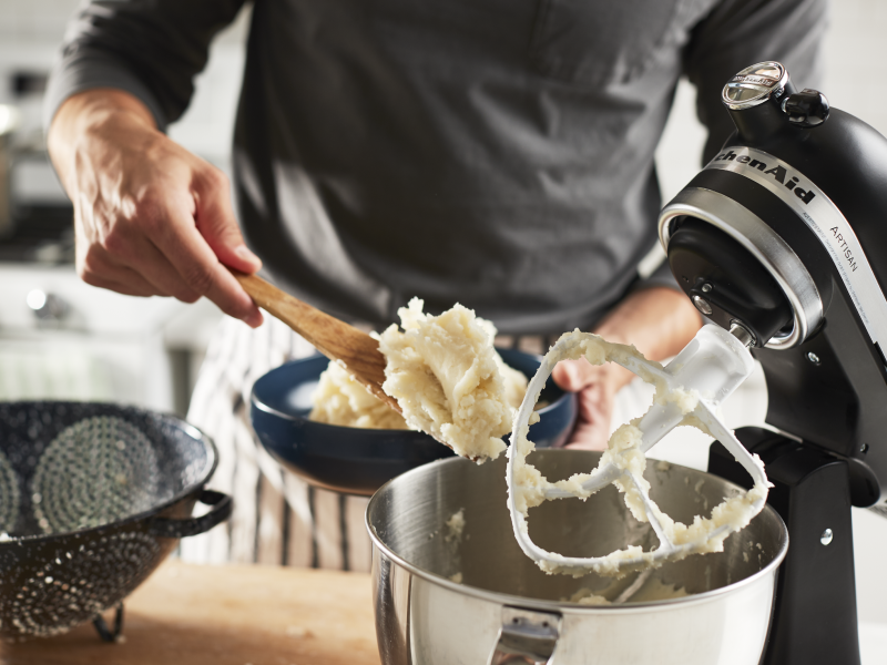 Man scooping mashed potatoes out of a stand mixer into a serving bowl Man scooping mashed potatoes out of a stand mixer into a serving bowl
