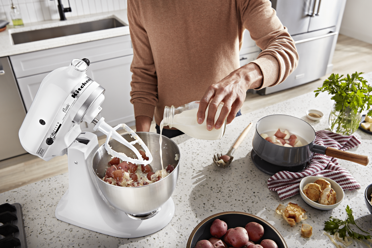 Man pouring milk into a stand mixer bowl of mashed potatoes Man pouring milk into a stand mixer bowl of mashed potatoes