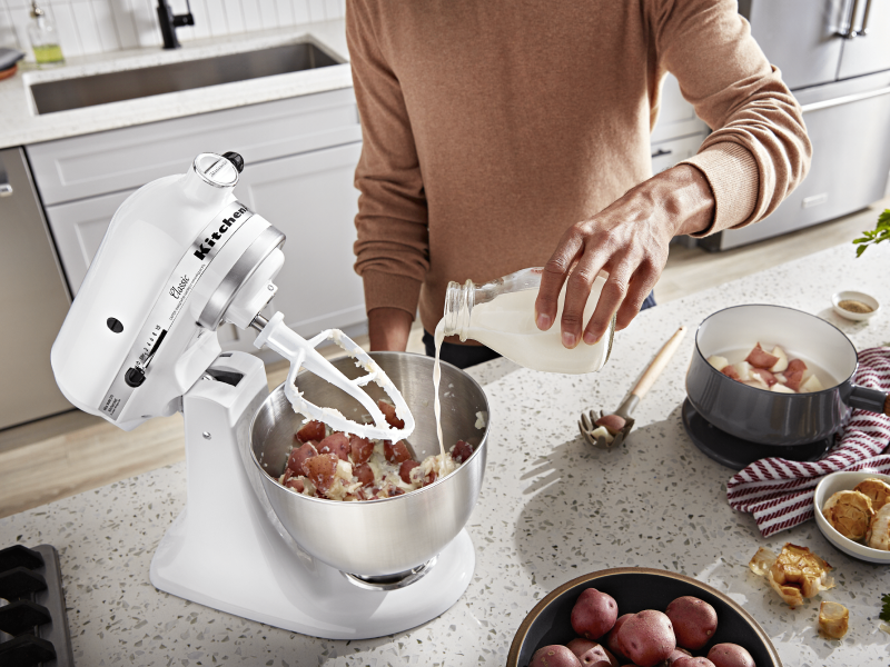 Man pouring milk into a stand mixer bowl of mashed potatoes Man pouring milk into a stand mixer bowl of mashed potatoes