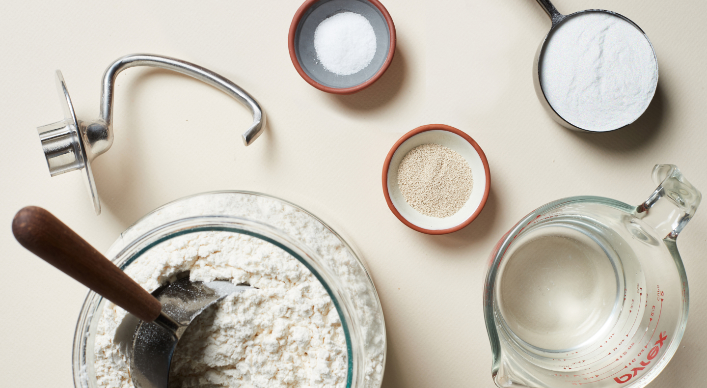 Ingredients for pizza dough next to a dough hook Ingredients for pizza dough next to a dough hook