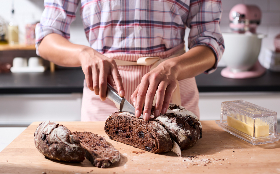 Maker using knife to cut slice of rye bread on cutting board Maker using knife to cut slice of rye bread on cutting board