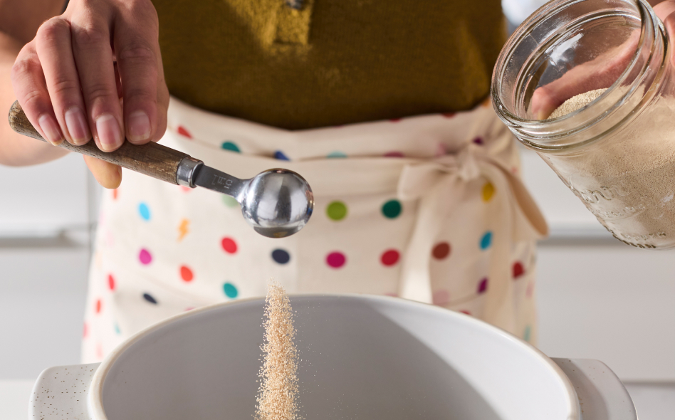 Maker tipping spoon full of yeast into a bread bowl Maker tipping spoon full of yeast into a bread bowl