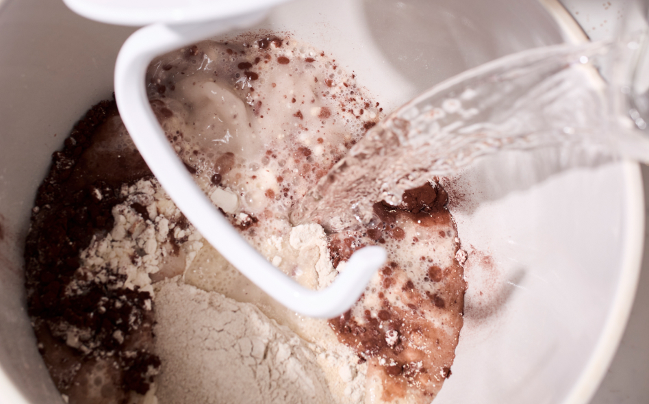 Close up of water being poured into mixing bowl with dry ingredients and dough hook Close up of water being poured into mixing bowl with dry ingredients and dough hook