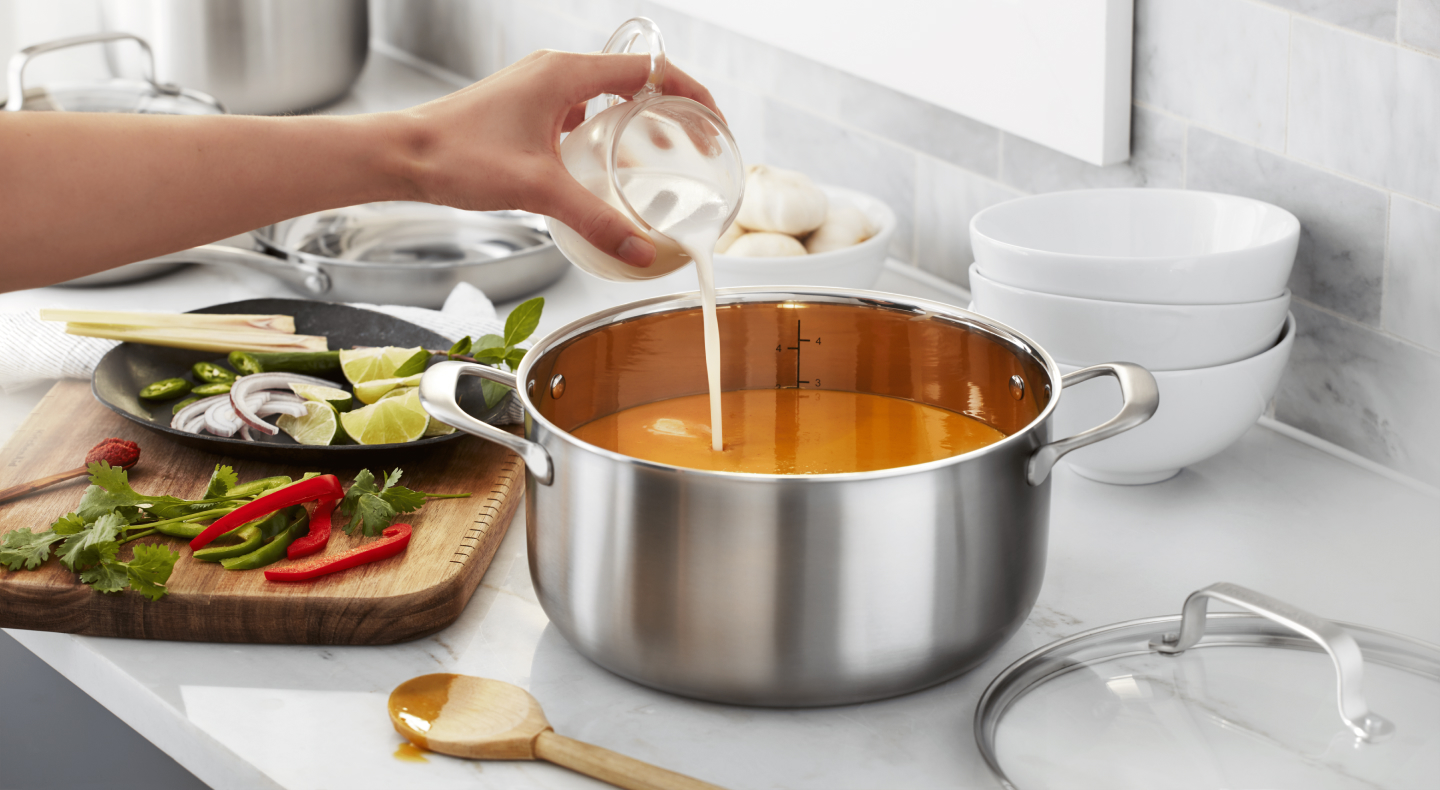 Person pouring cream into pot of soup Person pouring cream into pot of soup