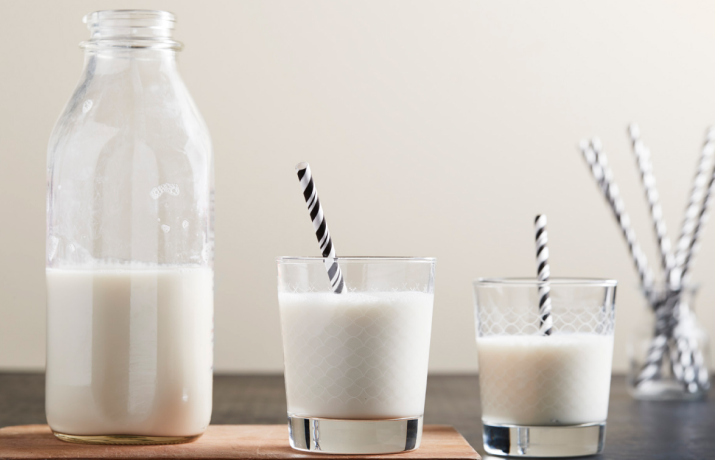 Two glasses of milk with black and white paper straws sitting on counter next to milk bottle Two glasses of milk with black and white paper straws sitting on counter next to milk bottle