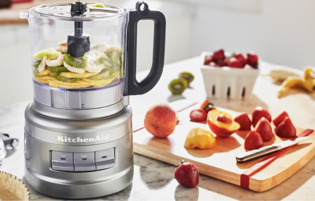Preparing to blend the perfect banana smoothie with bananas, kiwis, and pineapple slices layered in the bowl of a KitchenAid® food processor