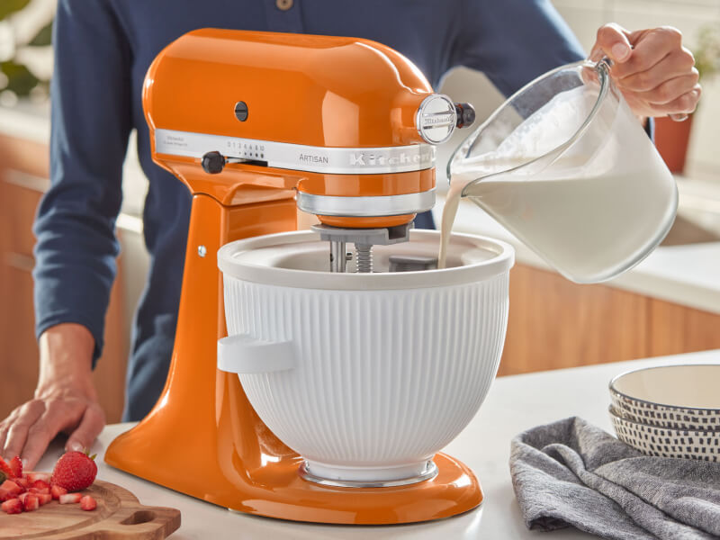 Hand pouring ice cream mixture into a KitchenAid® stand mixer bowl