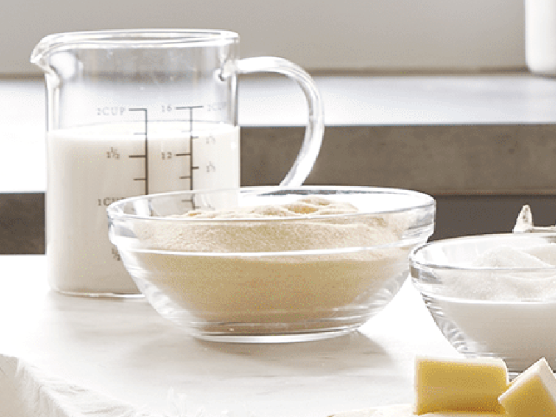 A measuring cup of milk and a bowl of yeast.