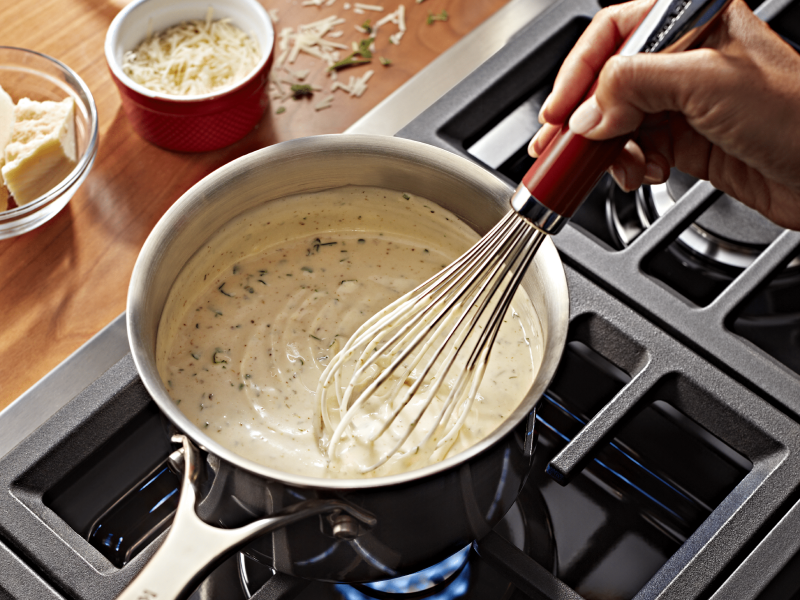 A person stirring homemade vegan queso on the stove.