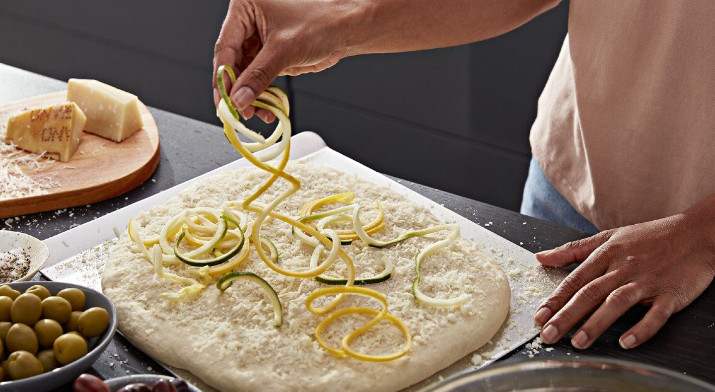 Woman strewing veggie noodles on pizza