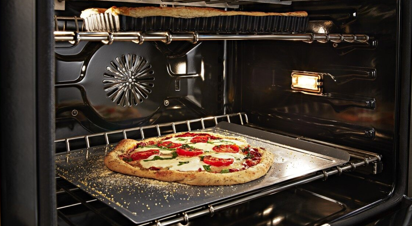 Artisan pizza baking in a convection oven with a dish baking on the rack above Artisan pizza baking in a convection oven with a dish baking on the rack above